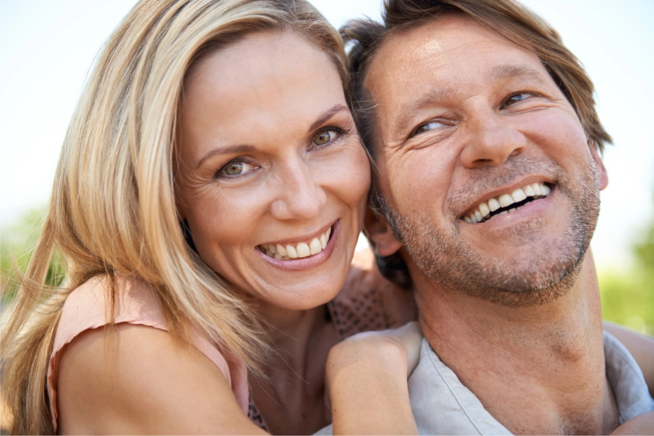 Pareja feliz mostrando sus sonrisas con dientes fijos, disfrutando de un momento alegre al aire libre, simbolizando los exitosos resultados de la implantología inmediata en nuestra clínica Pérez Paniagua.